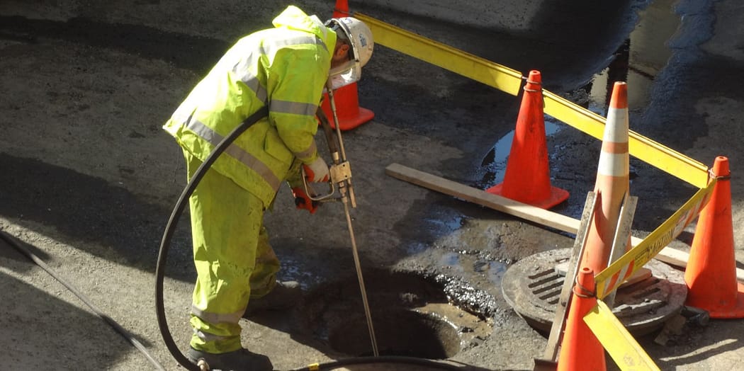 Worker cleaning manhole with hose
